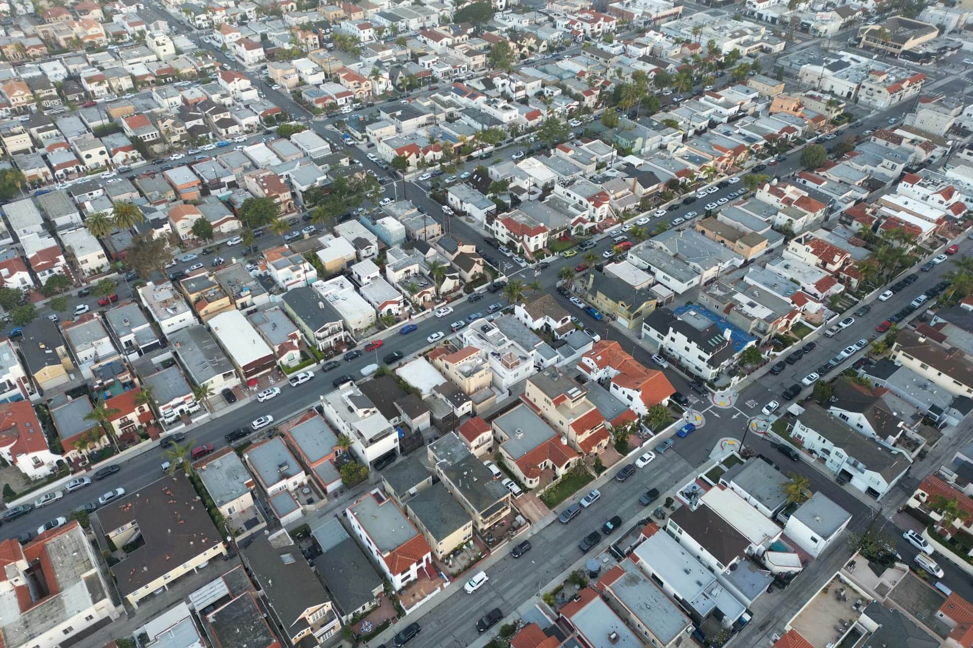 Aerial view of a dense residential neighborhood of closely packed houses, palm trees and parked cars along intersecting streets